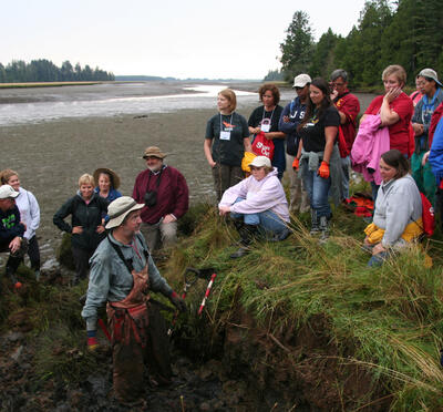 CEETEP participants learn about tsunami geology from US Geological Survey research, Brian Atwater. Niawiakum River, Washington. Participants are gathered at the edge of the salt marsh as Brian explains the layers observed below.